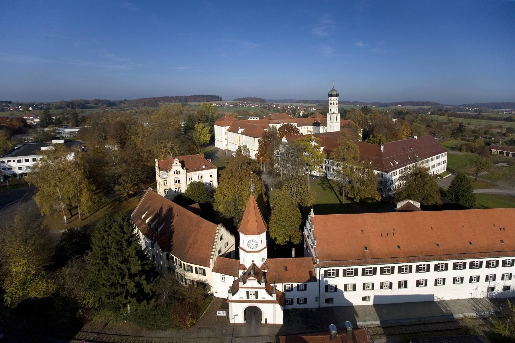 Luftbild mit Blick auf die Anlage von Kloster Schussenried mit der Toranlage im Vordergrund und der Klosterkirche im Hintergrund 