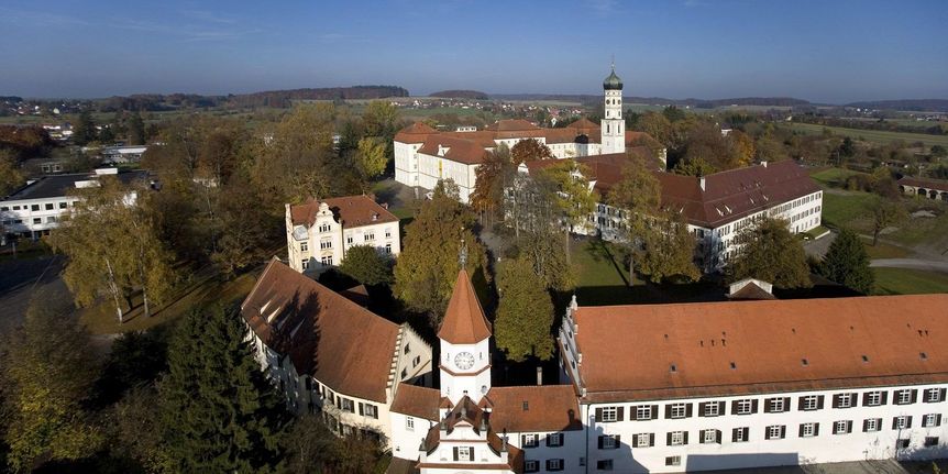 Luftbild mit Blick auf die Anlage von Kloster Schussenried mit der Toranlage im Vordergrund und der Klosterkirche im Hintergrund 