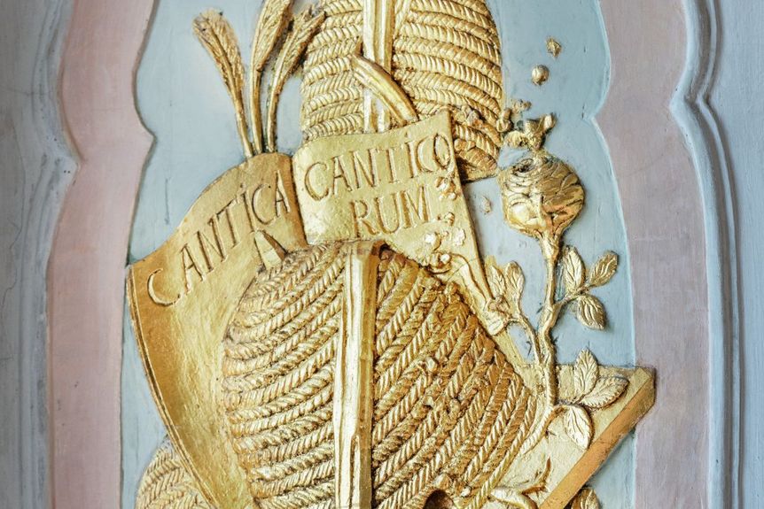 Stuckrelief an einer Fensterlaibung: Zu sehen sind Bienenstöcke, Honig, Blüten und Schriftstücke 